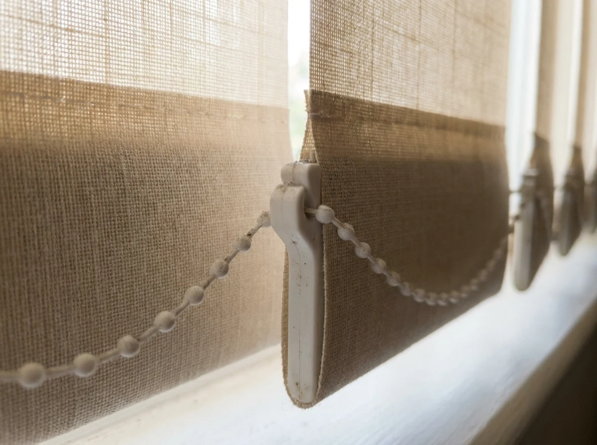 Close detail of a vertical blind vane clip and bottom chain, indoor light